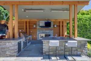 Outdoor kitchen with fireplace, TV, and bar seating.
