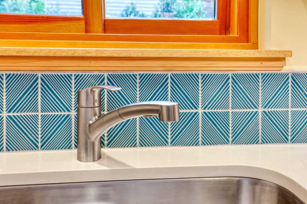 Stainless steel faucet over teal patterned backsplash