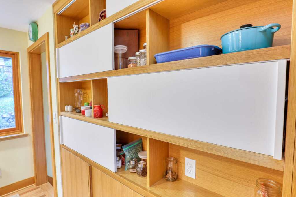 Open wooden kitchen shelf with colorful cookware and jars