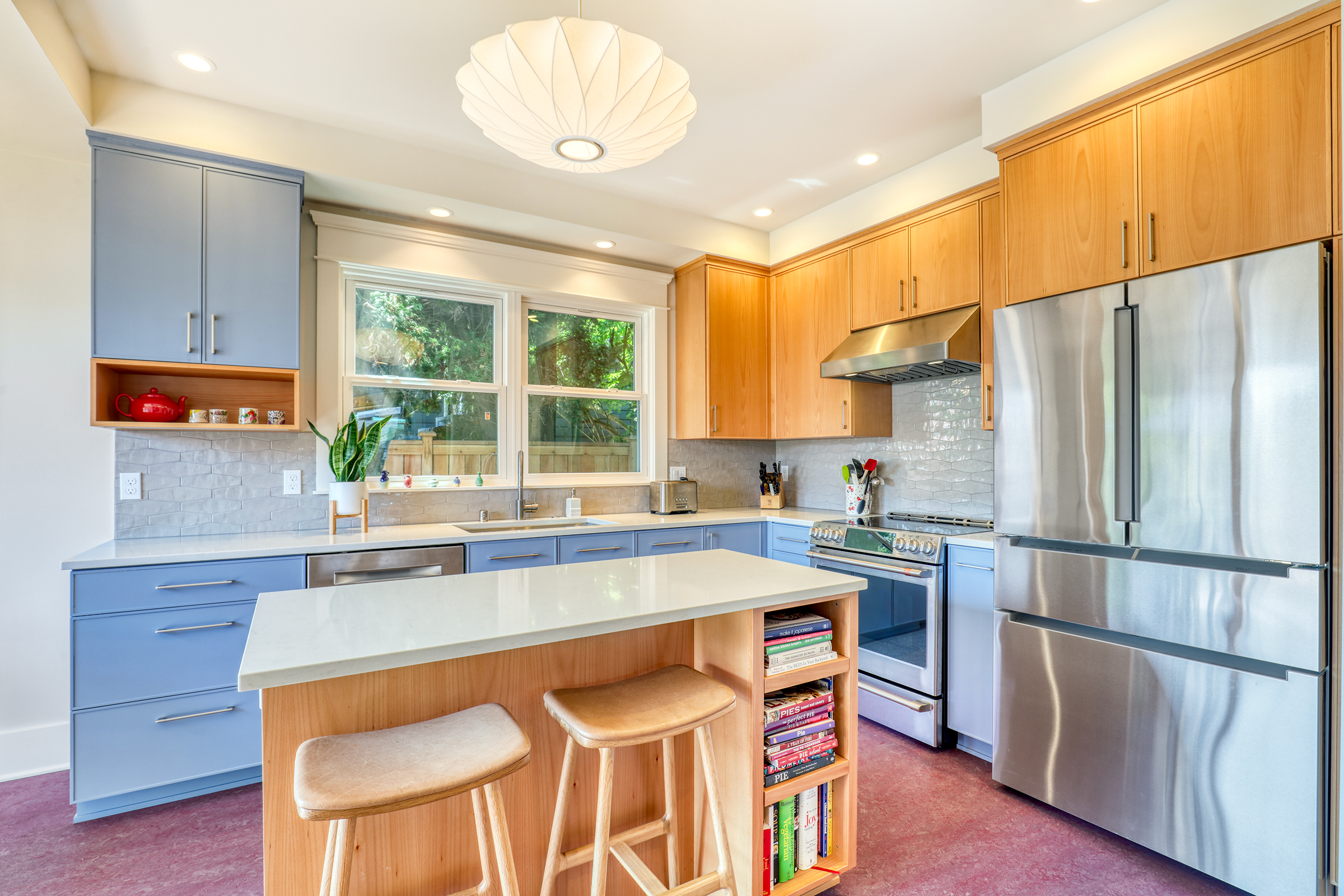 A modern kitchen remodel showcasing current design trends, featuring periwinkle blue lower cabinets, warm natural wood upper cabinets and island, white quartz countertops and textured subway tile backsplash.