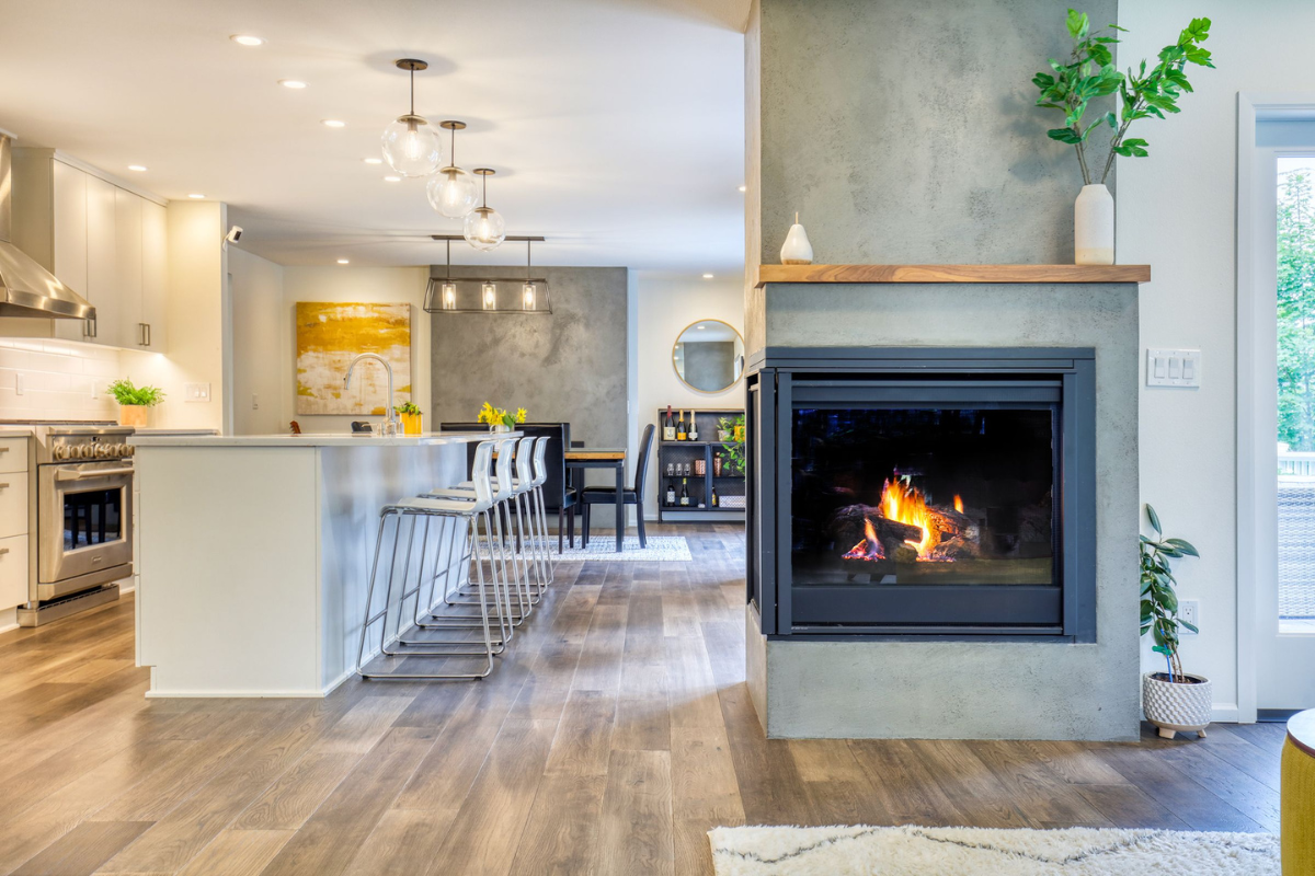 Open-concept kitchen and living space with concrete fireplace surround and warm hardwood floors. A finished result from the design build process explained through Schulte's integrated approach.