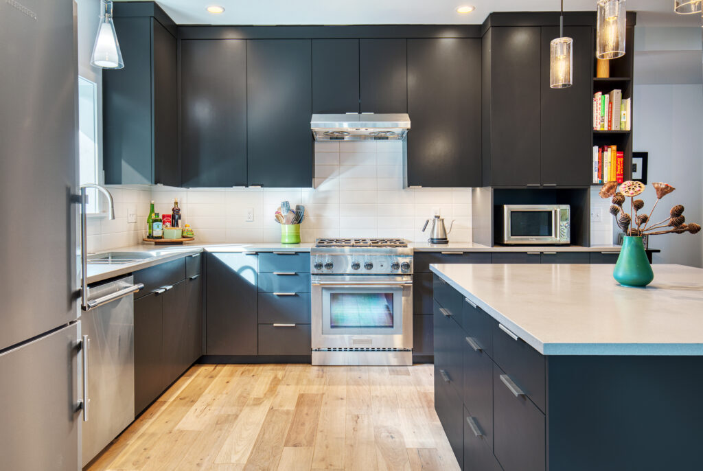 Modern kitchen renovation featuring floor-to-ceiling matte navy cabinetry, white quartz countertops, large-format tile backsplash, and professional stainless appliances.