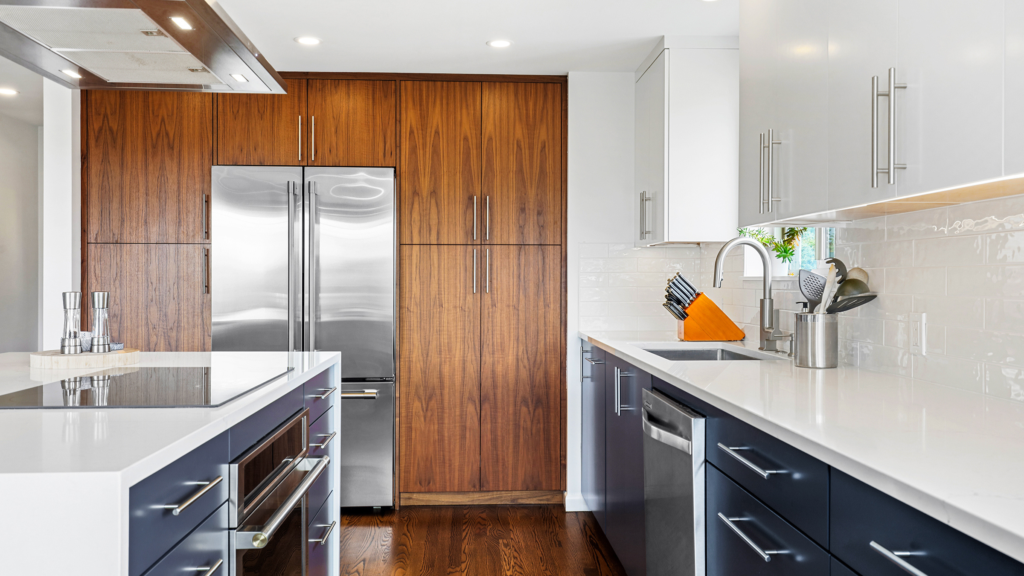 Modern two-tone kitchen from this Seattle remodel with walnut wall cabinetry, integrated stainless appliances, and a navy island.