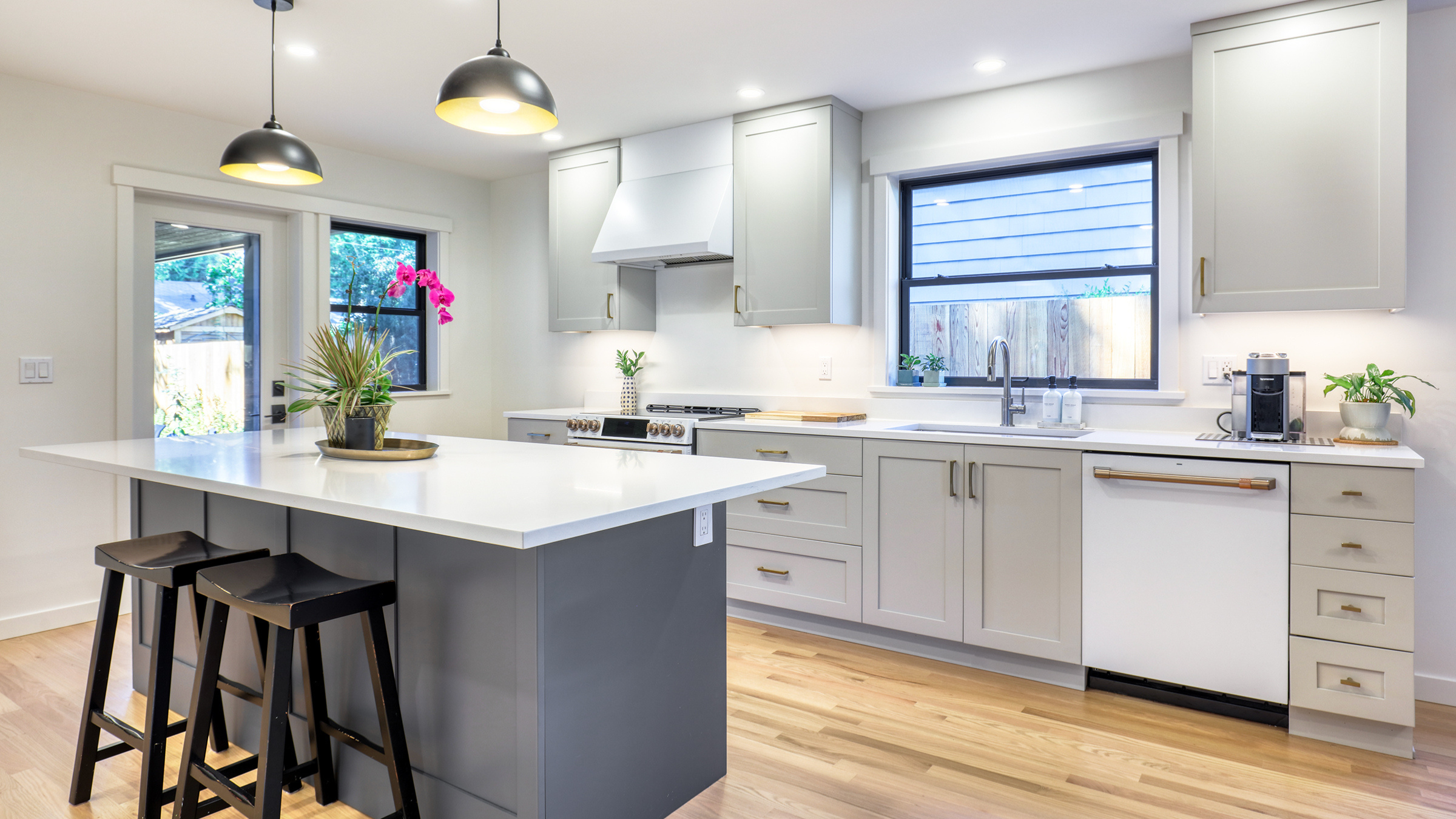 Kitchen remodel Seattle project featuring light gray shaker cabinets, a two-tone island with white quartz countertop, brass hardware, and black pendant lighting.