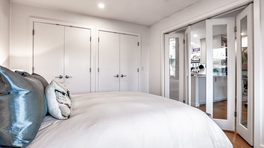 Bedroom with white closet doors and mirrored bifold doors opening onto the kitchen remodel in Queen Anne beyond.