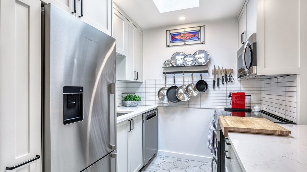 Galley kitchen remodel in Queen Anne with white shaker cabinets, stainless appliances, a skylight and cookware hung on a wall rail.